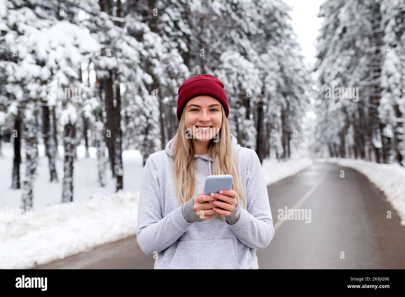 Donna sportiva in piedi in natura durante la giornata invernale innevata e messaggio di SMS. Fitness invernale, telecomunicazioni, fitness all'aperto Foto Stock