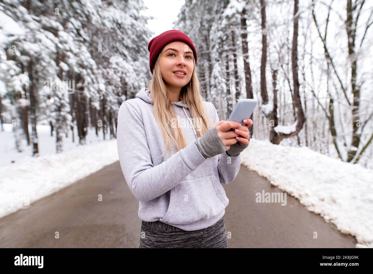 Donna sportiva in piedi in natura durante la giornata invernale innevata e messaggio di SMS. Fitness invernale, telecomunicazioni, fitness all'aperto Foto Stock
