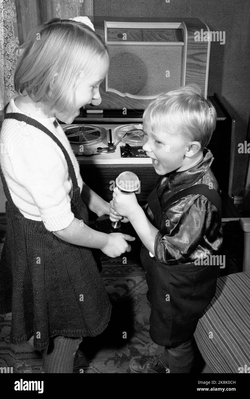 OSLO Desember 1949. Magnetofonen introduses i Norge. DET er firmaet Proton som har enerett på navnet Magnetofon. Sere blir maskinen kjent under en rekke navn, som båndspiller, lydbånd, båndopptaker e spolebåndspiller. Å kunne spille inn og bevare inntrykk fra barnas første år var mange foreldres drøm. Il suo er det al fienile som prøver ut båndspilleren i hjemmet med en ellevill cantato. Gutt og jente som synger i en mikrofon. Foto: Sverre A. Børretzen / Aktuell / NTB Oslo Dicembre 1949: Il Magnetofon viene introdotto in Norvegia. L'azienda Proton aveva i diritti per il marchio Magnetofon, era tardi Foto Stock