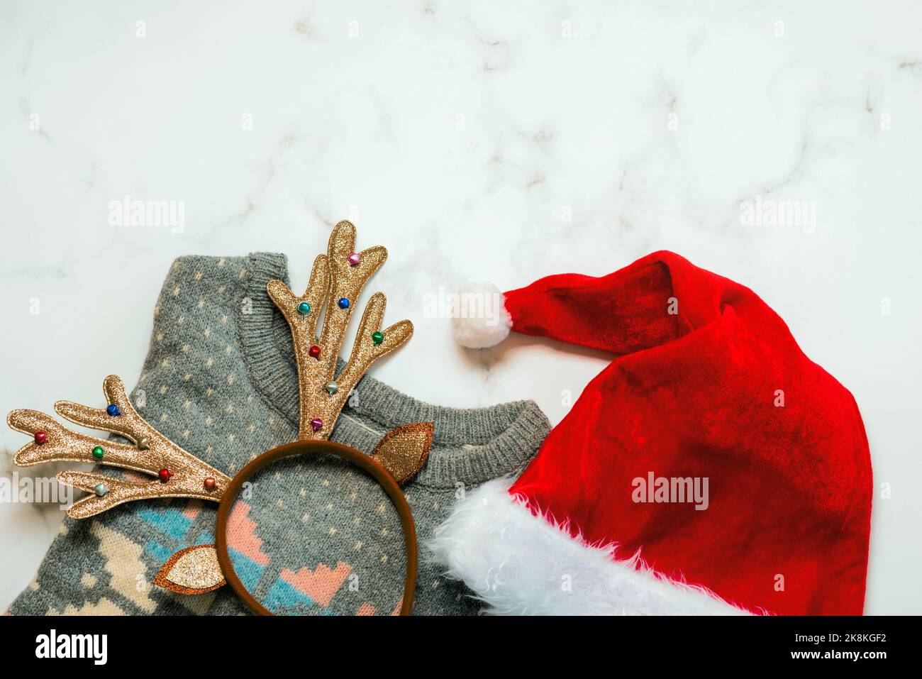 Buon Natale. Vista dall'alto del maglione di natale con corna di cervi e cappello di Babbo Natale su un tavolo di marmo Foto Stock