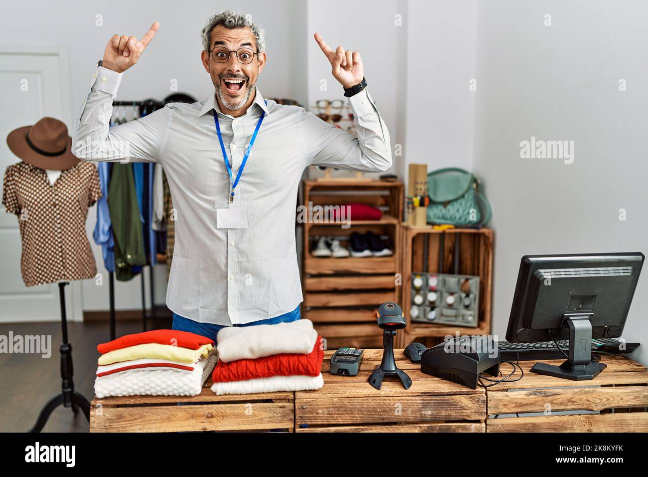Uomo ispanico di mezza età che lavora come manager al negozio boutique sorridendo stupito e sorpreso e indicando con le dita e le braccia sollevate. Foto Stock