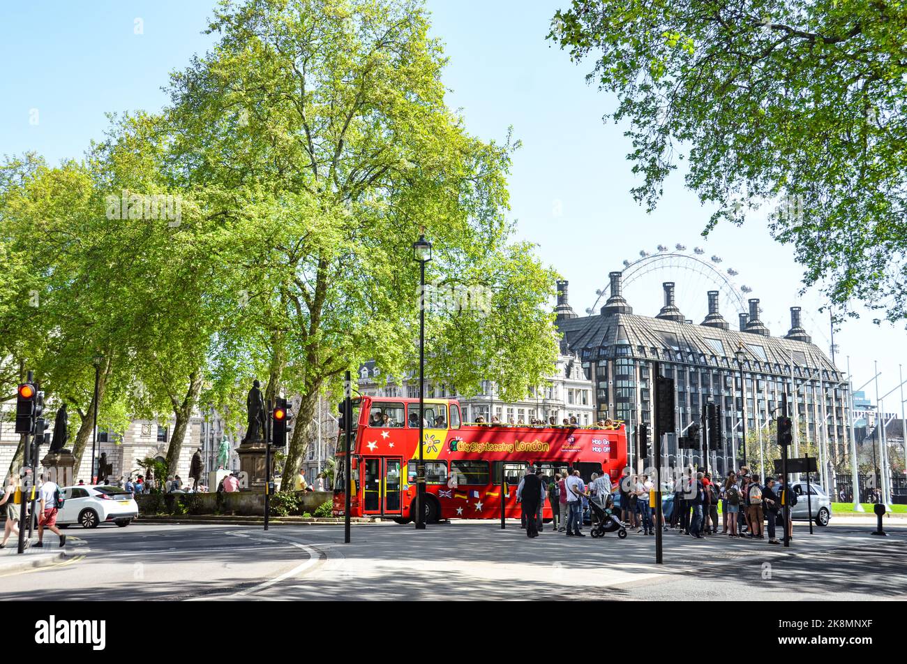Persone in piedi per le strade di Londra, Regno Unito con un autobus rosso, alberi e un edificio sullo sfondo. Foto Stock