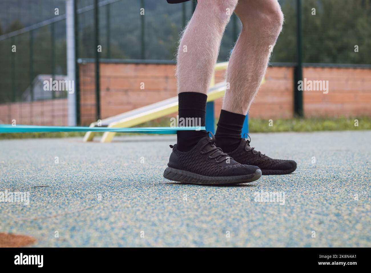 Allenatore di fitness esercita la metà inferiore del corpo al mattino su un campo di allenamento all'aperto con l'aiuto di espansori e fasce di gomma. Caviglia, ca Foto Stock