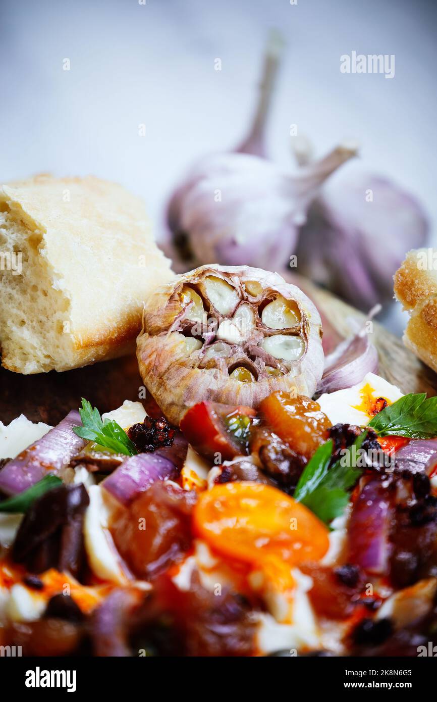 Bulbo d'aglio arrostito in olio e servito con un saporito pannello di burro e baguette. Messa a fuoco su bulbo con primo piano e sfondo sfocati. Foto Stock