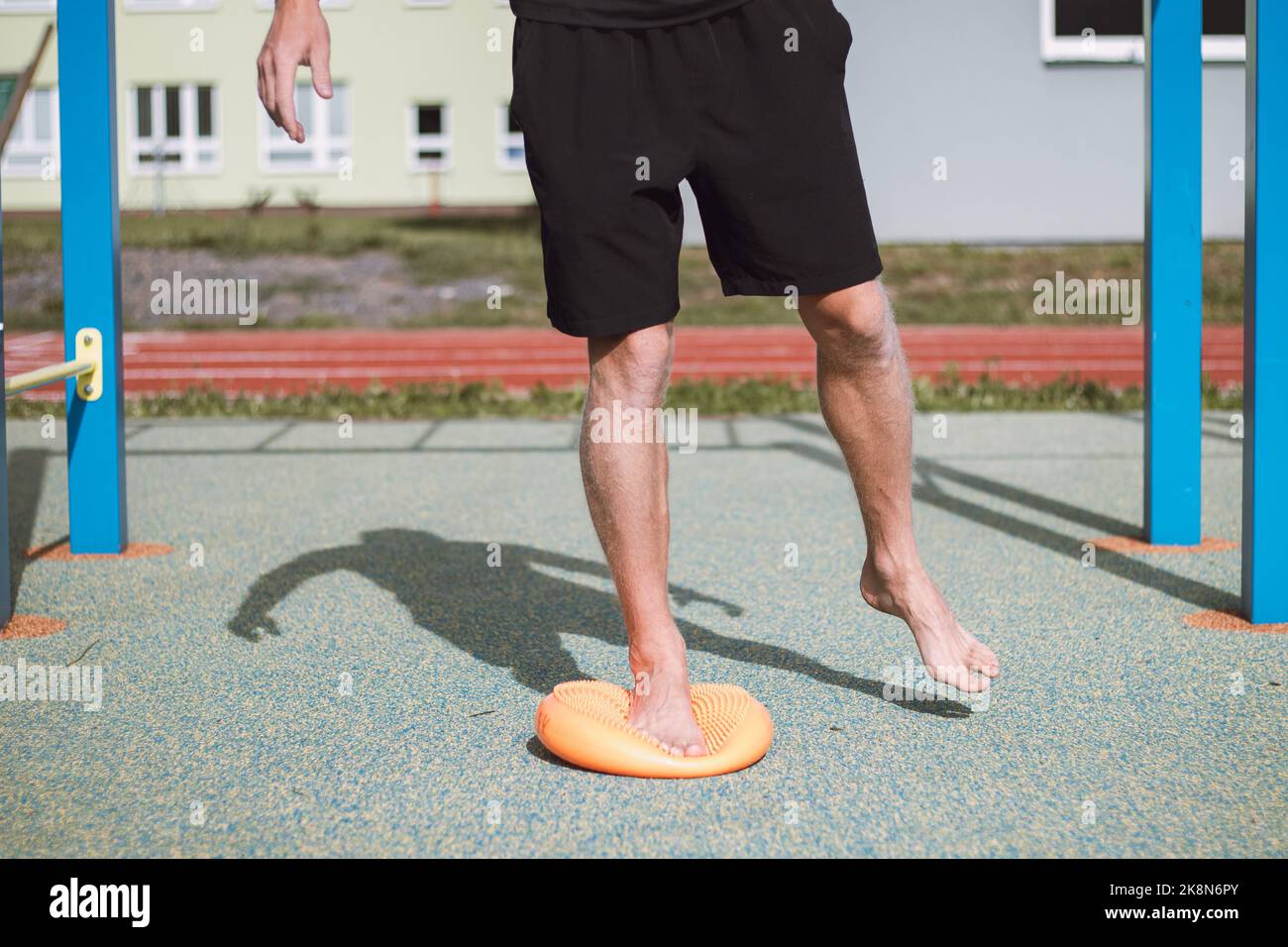 Un atleta professionista rinforza la caviglia su uno speciale obiettivo arancione pieno d'aria. Esercizio di riabilitazione dopo la caviglia. Area wourkout all'aperto. Foto Stock