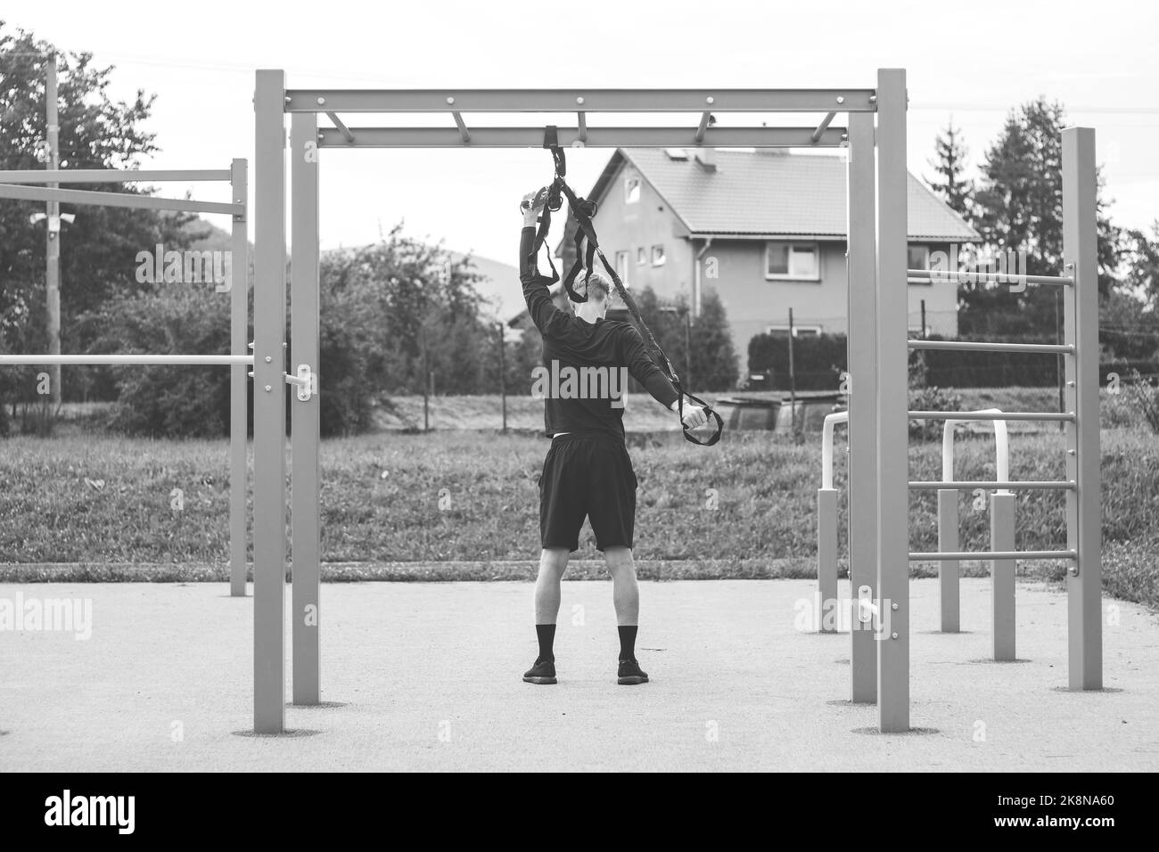 Un atleta professionista allunga e rinforza braccia, spalle, muscoli pettorali e muscoli della schiena intorno alla colonna vertebrale con le cinghie fitness TRx. Suppor Foto Stock