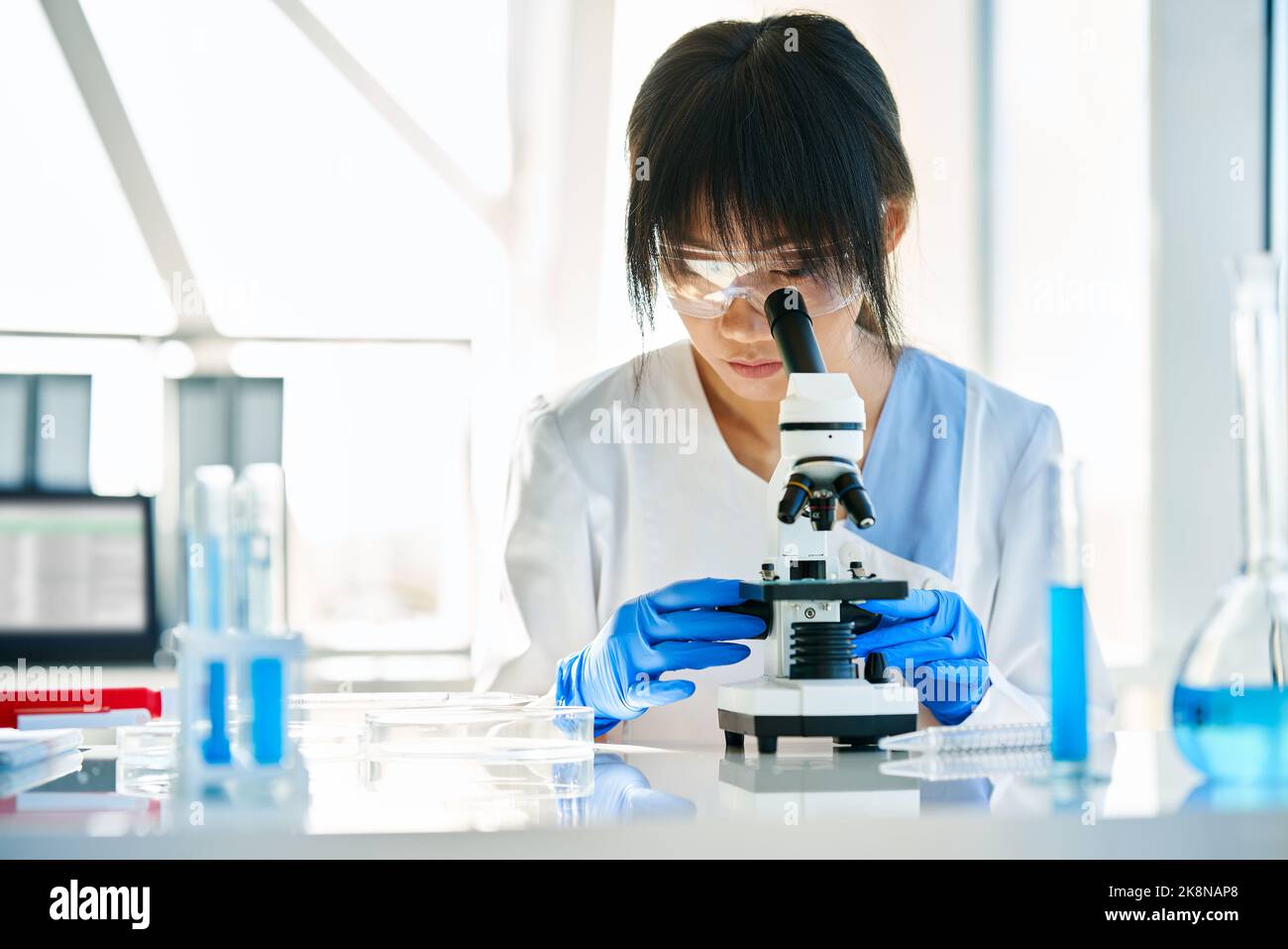 Uno scienziato che guarda attraverso un microscopio lavorando alla ricerca medica in laboratorio scientifico Foto Stock