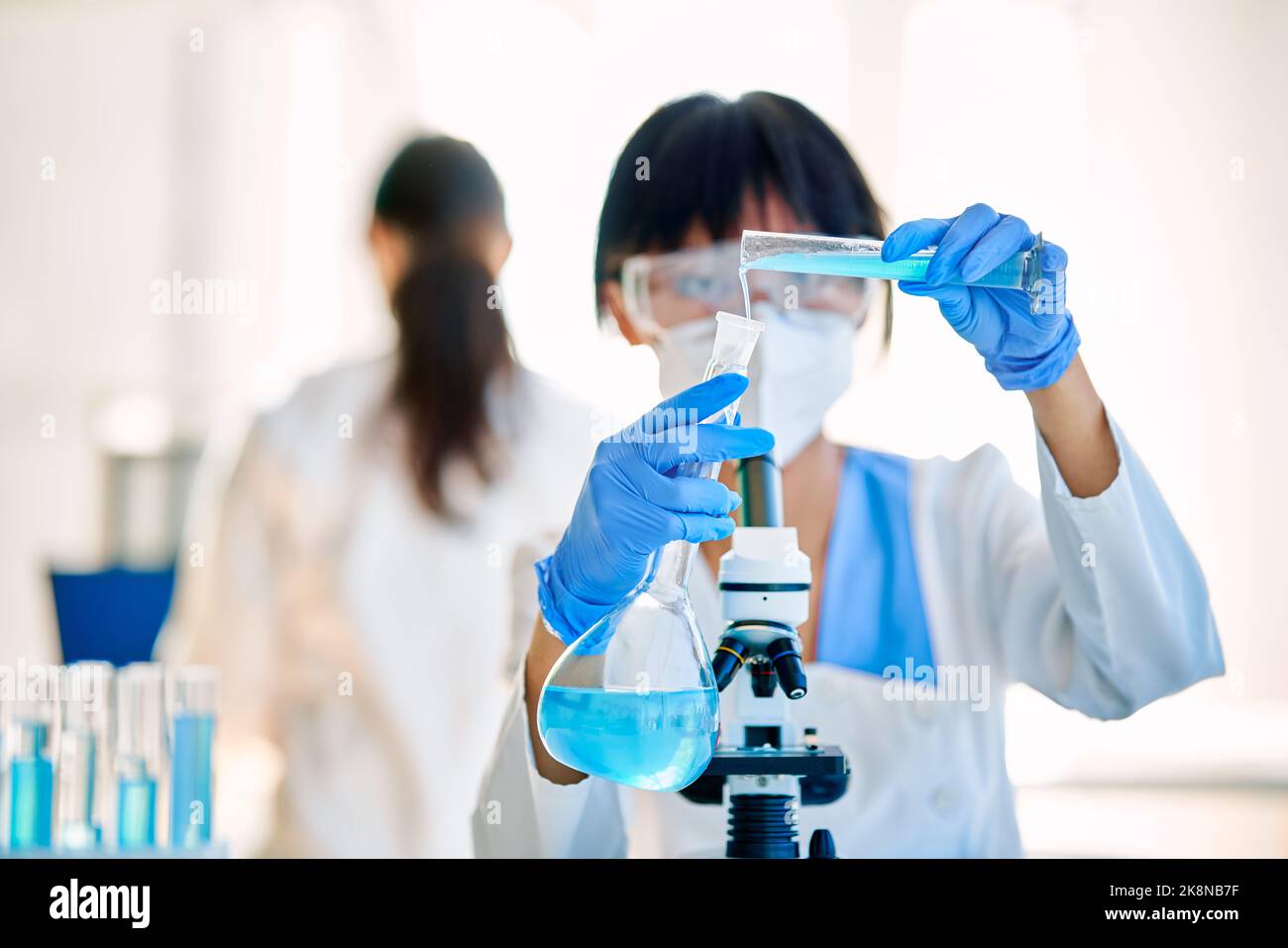 Scienziato femminile che effettua ricerche versando il reagente in provette che lavorano in moderni laboratori medici. Sviluppo di medicina, biotecnologia, microbiologia Foto Stock