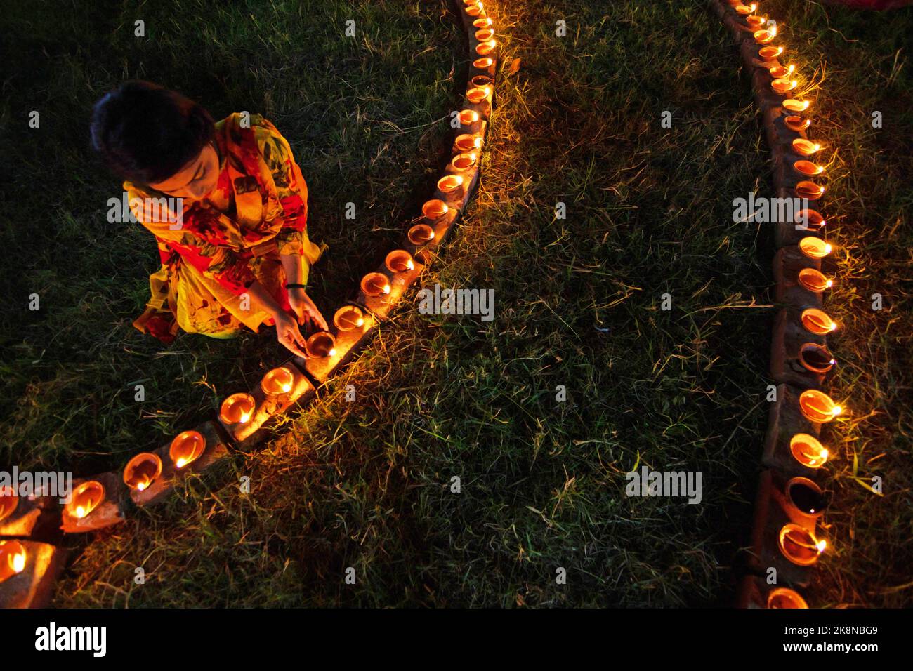 Narayanganj, Dhaka, Bangladesh. 24th Ott 2022. I devoti indù illuminano ''Diyas'' (lampade di terra) su un Rangoli, una cornice di motivi decorati, come parte dei festeggiamenti di Diwali in un tempio locale a Narayanganj, Bangladesh. Molte lampade o candele ad olio leggero per simboleggiare una vittoria della luce sulle tenebre, e fuochi d'artificio sono accesi come parte delle celebrazioni. Il festival si svolge ogni anno secondo il calendario lunare indù. Credit: ZUMA Press, Inc./Alamy Live News Foto Stock