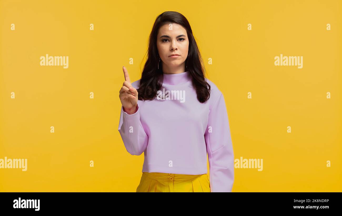 giovane donna in felpa viola puntando con il dito e guardando la macchina fotografica isolata sul giallo Foto Stock