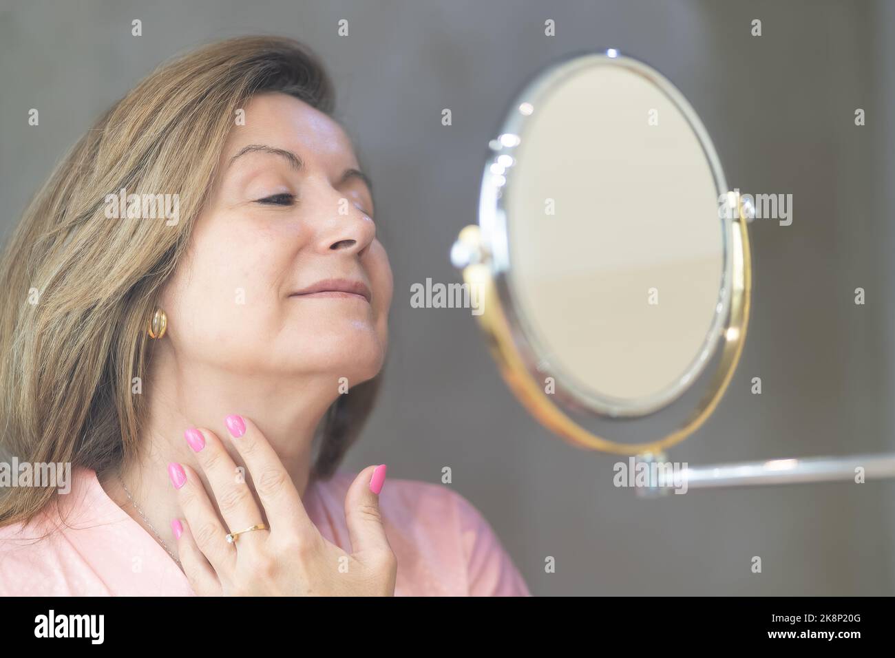 Donna anziana che si prende cura della sua pelle di fronte a uno specchio in bagno. Foto Stock