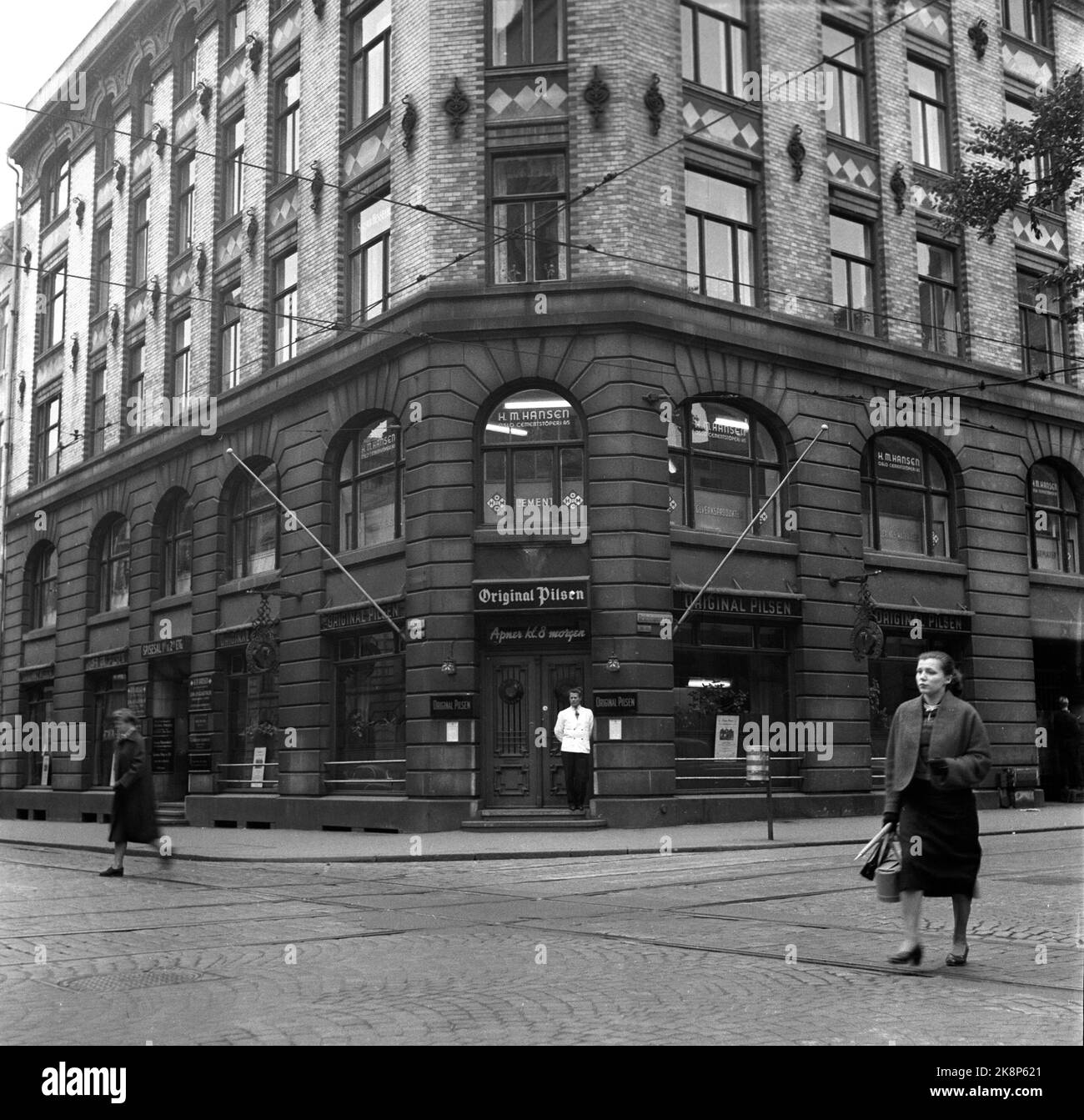 Oslo 19550922. Il nightclub Pilsen originale. In questo periodo si trovava all'angolo tra porta Dronningens e Tollbugata. Edificio semplice a 5 piani di storia. I due piani inferiori sono suddivisi in superfici verticali divise in mattoni intonacati. Un cameriere della giacca bianco si trova all'ingresso. Due donne passano Tollbugaten. Anche le guide del tram e la sospensione elettrica per i tram caratterizzano l'immagine. Foto: Archivio NTB / NTB Foto Stock