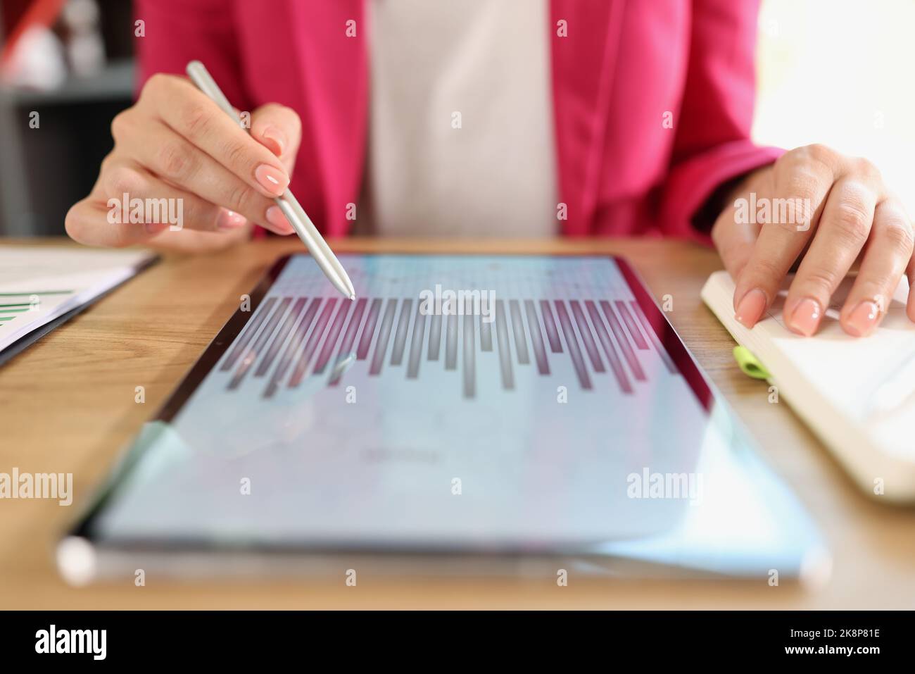 Donna seduta al tavolo e che indica lo schermo del tablet con grafico Foto Stock