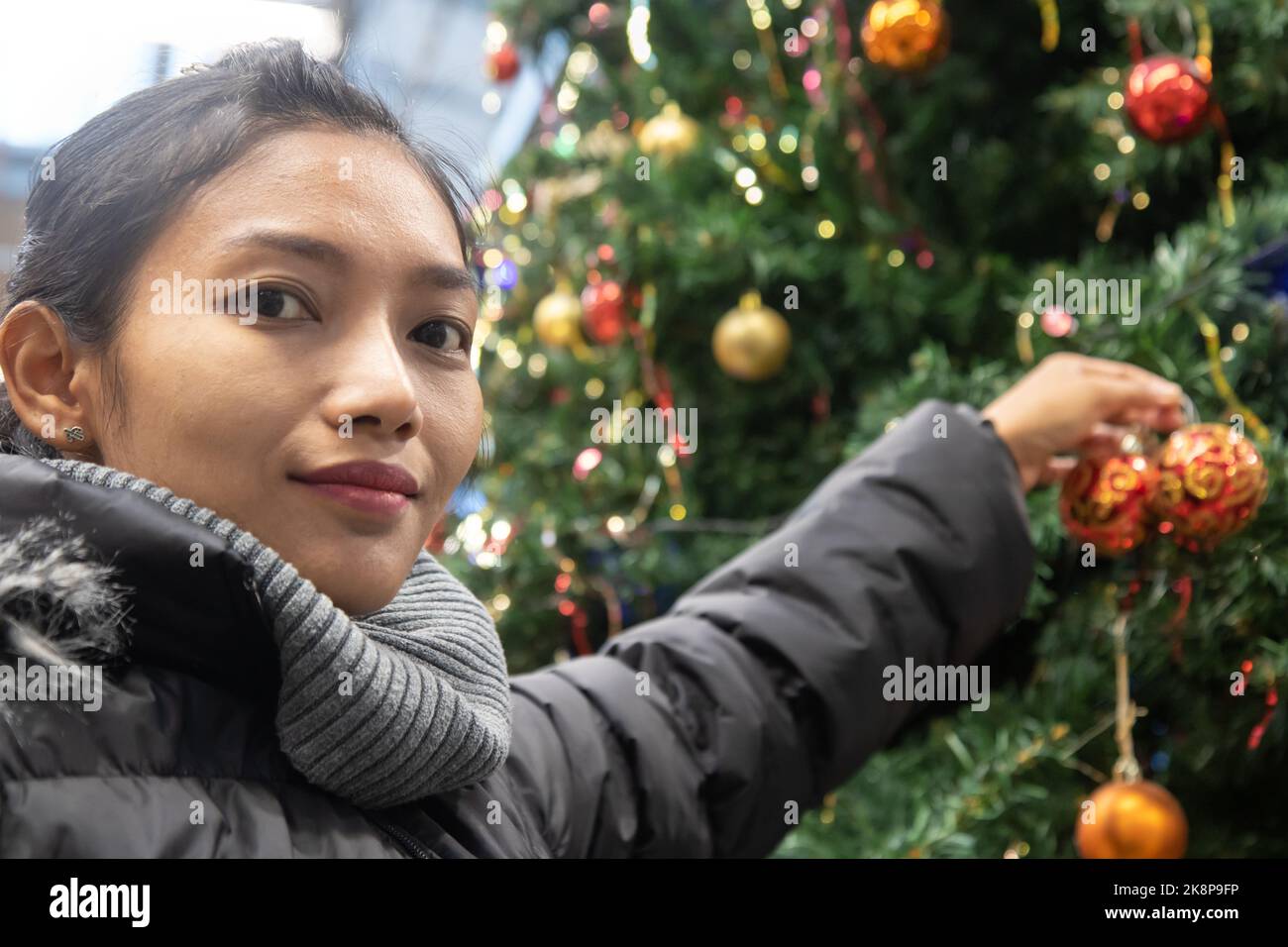 Una giovane donna in giacca invernale decorare un grande albero di Natale Foto Stock