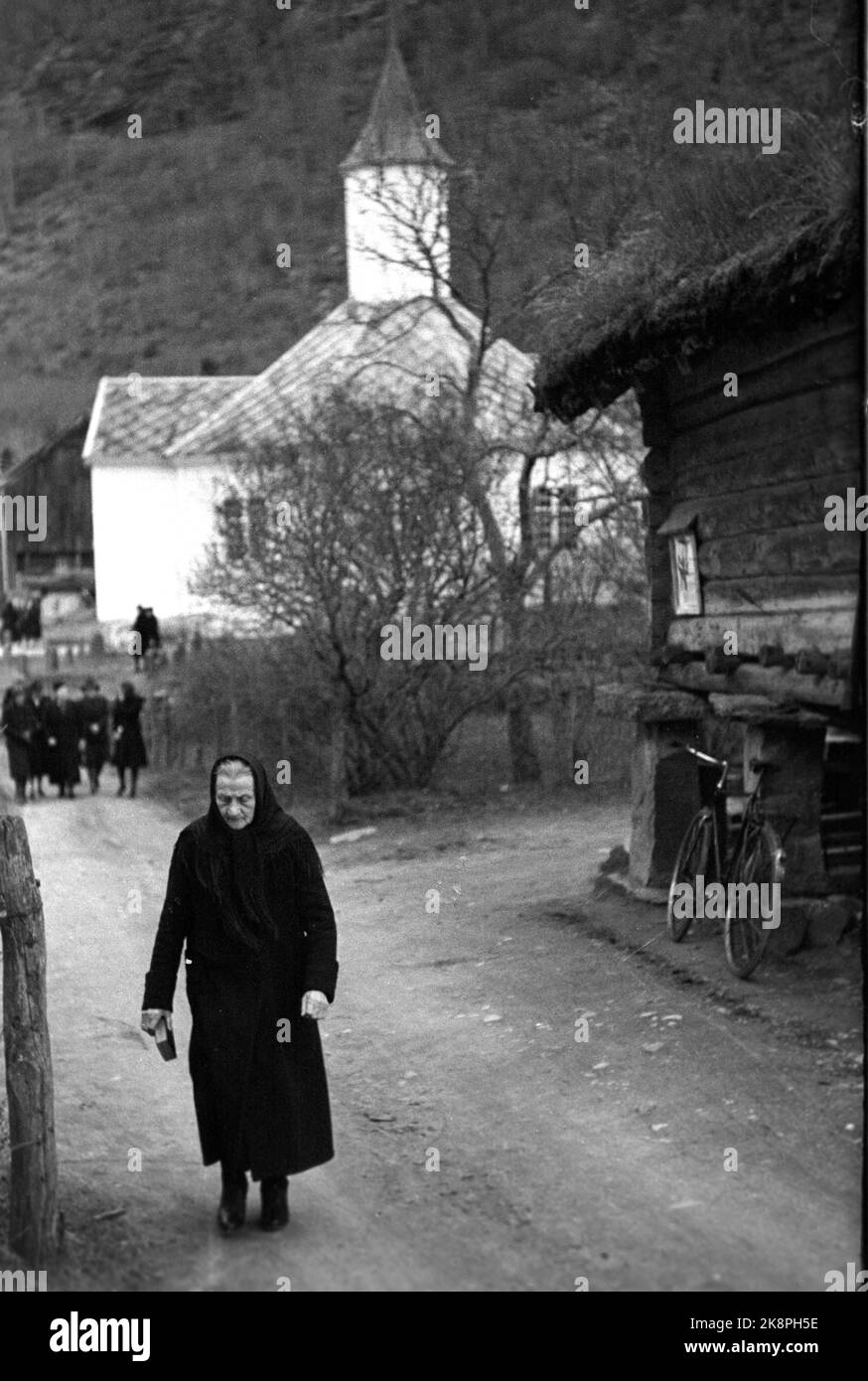 Loen 1947 poco più di 10 anni dopo il grande incidente di gara, la vita è tornata nei villaggi intorno a Loen. Il servizio è finito nella chiesa in legno di Loen, risalente a 100 anni fa. Vecchia donna vestita di nero sulla via di casa dopo il servizio. La chiesa sullo sfondo. Foto: TH. Scotaam / corrente / NTB Foto Stock