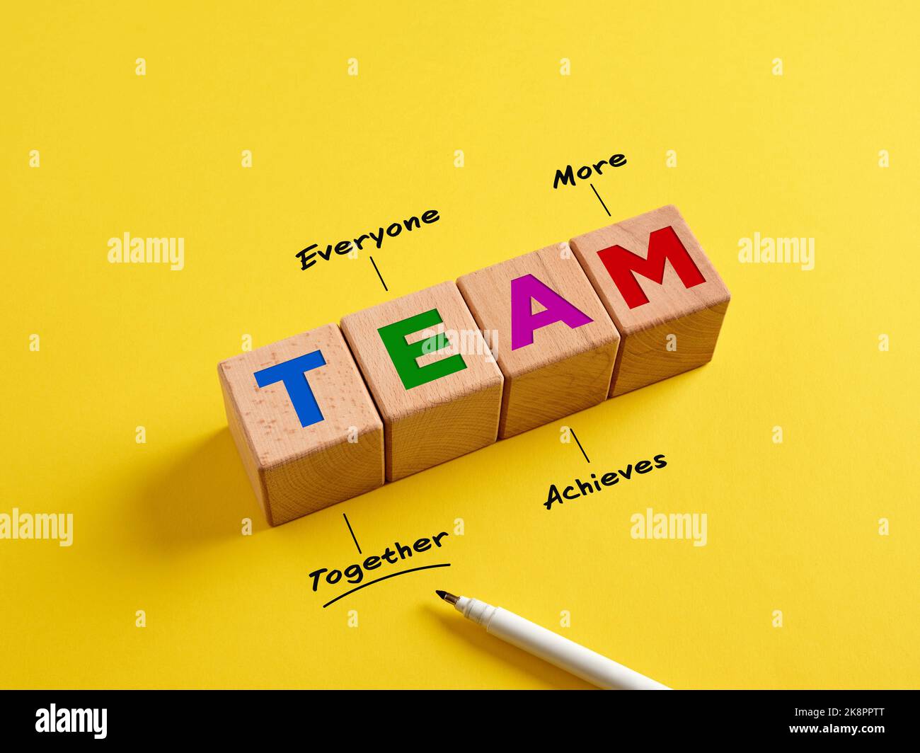 Concetto di sinergia tra business e lavoro di squadra. La parola Team su cubi di legno e acronimo con la definizione di scrittura a mano (insieme tutti ottiene di più). Foto Stock