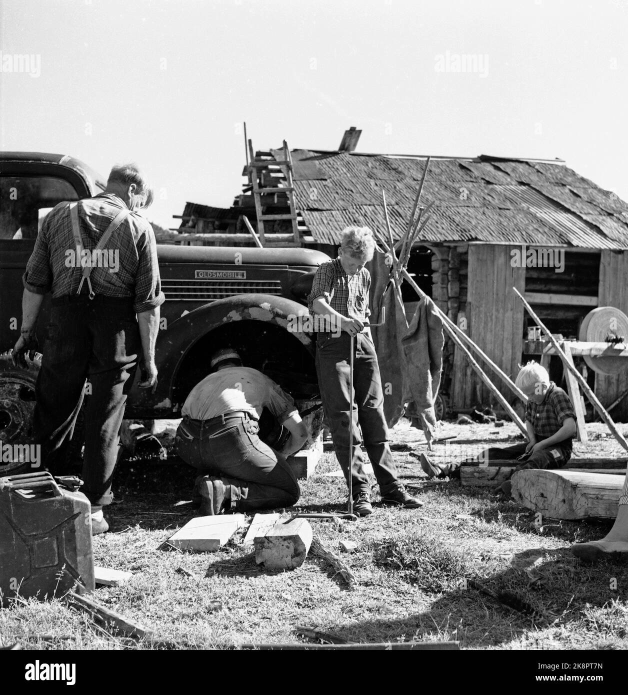 Flatdal in Telemark, agosto 1959. Fjellgården Ekre si trova a 600 metri sul livello del mare e in un terreno così accidentato che 'nessuno penserebbe che nessuno possa bu'. Ciò che occorre fare deve essere fatto di gran lunga. Qui, il padre e i figli della fattoria riparano il vecchio camion. Sullo sfondo, il vecchio fienile che ha più di 200 anni. Foto: Aage Storløkken / corrente / NTB Foto Stock