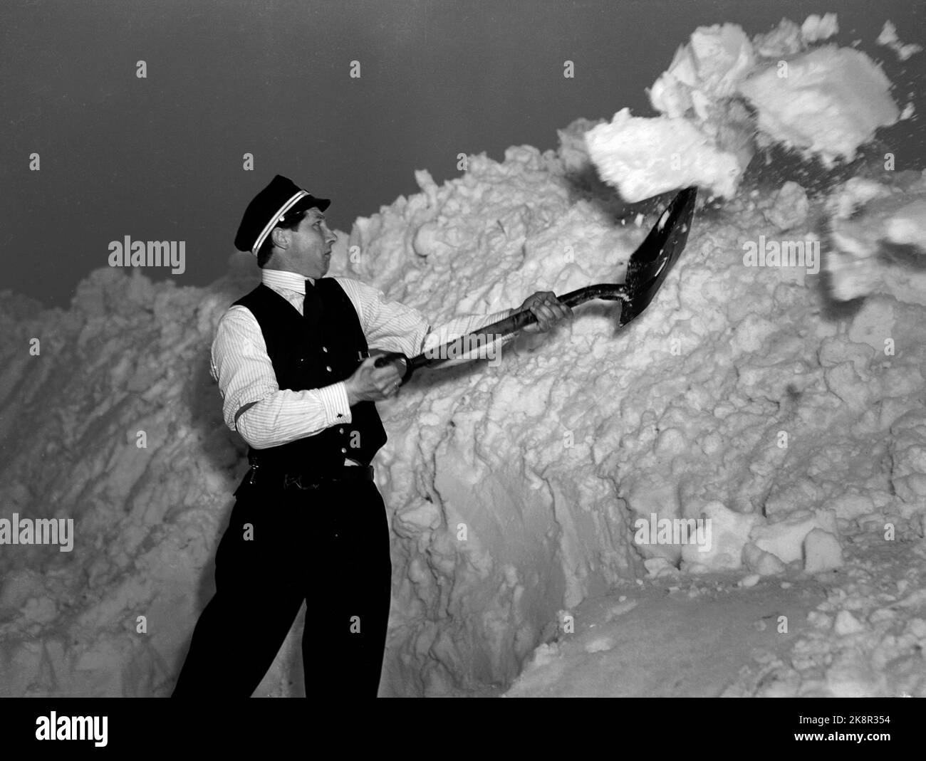 Nelaug stazione 19510207: Forte nevicata sulla parte meridionale del paese ha creato caos nel traffico ferroviario. In totale, cinque treni sono rimasti bloccati nelle masse di neve alle stazioni di Helldalsmo e Nelaug, e i passeggeri hanno dovuto trascorrere la notte in treni ghiacciati. Tutti gli uomini che lavorano alla sgombero della neve. Ecco un NSB noleggiato neve con una pala. Foto: NTB / NTB Foto Stock
