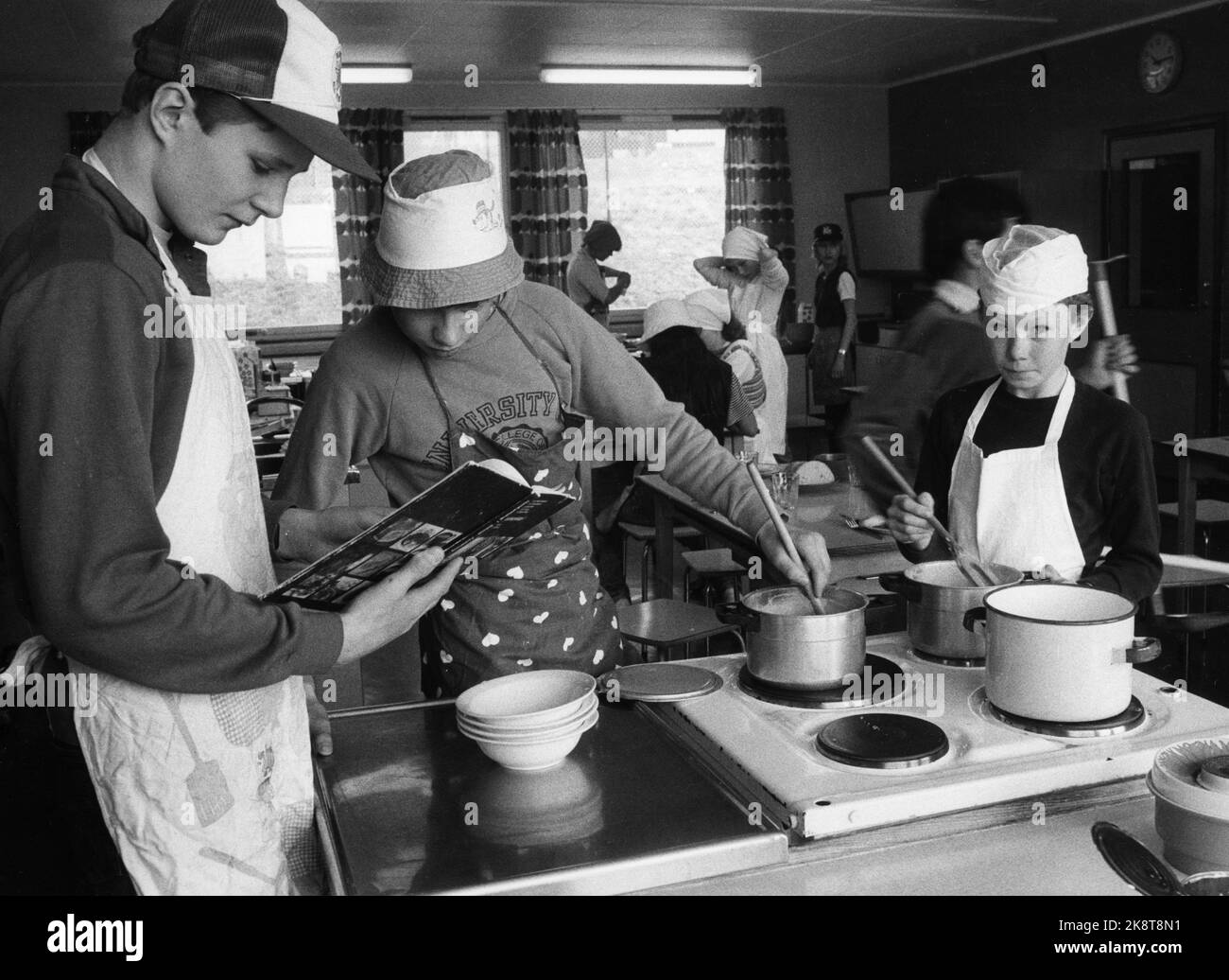 Oslo 19830429. Scuola di cucina a scuola Rødvet. I propri gruppi di ragazzi e ragazze in classe nella cucina della scuola. Gli studenti hanno il copricapo e i grembiuli adeguati. Si alza alla stufa e si agita in pentole (pentole di alluminio e pentole di smalto). Un lettore da un ricettario. Foto: NTB / NTB Foto Stock