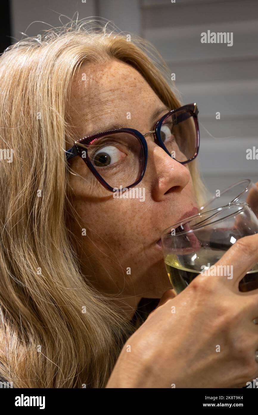 Donna bionda con bicchieri e pazzo guardare bere da due bicchieri di vino contemporaneamente. Concetto di abuso di alcool nei giovani. Foto Stock