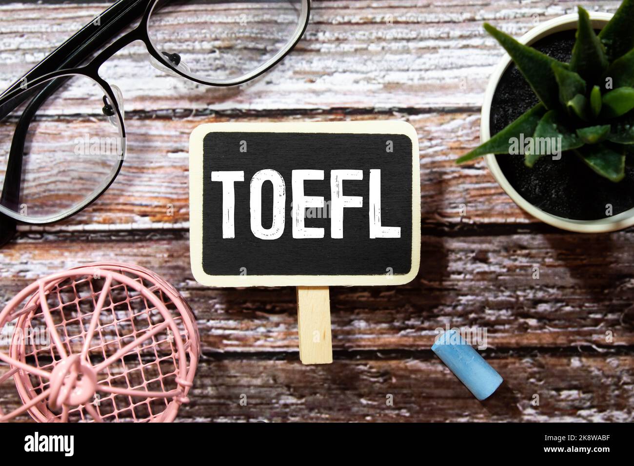 Esame di prova in inglese TOEFL scritto in quaderno nero con clip, marcatori e note attorno alla tabella blu. Foto Stock