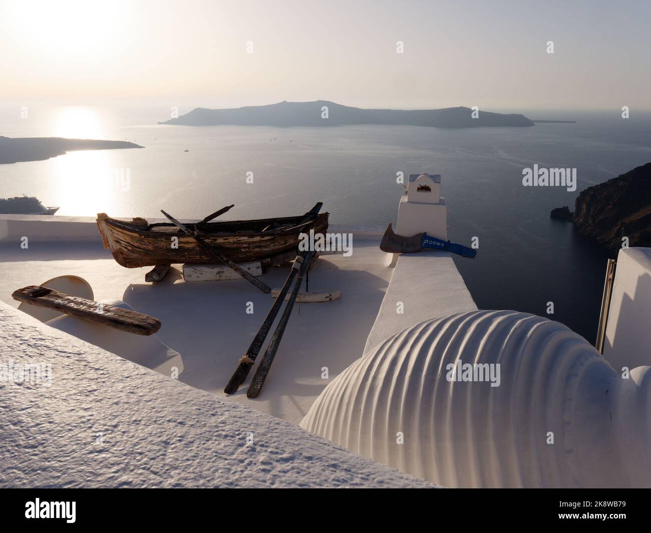 Vista su Firostefani al tramonto sulla Caldera. Isole Cicladi greche di Santorini nel Mar Egeo. Imbarcazione in legno sul tetto in primo piano. Foto Stock