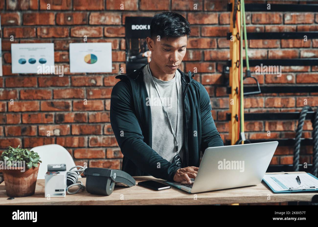 HES si è dedicato alla gestione efficace di questa palestra. Un bel giovane istruttore di fitness maschile che usa un computer portatile mentre lavora in palestra. Foto Stock