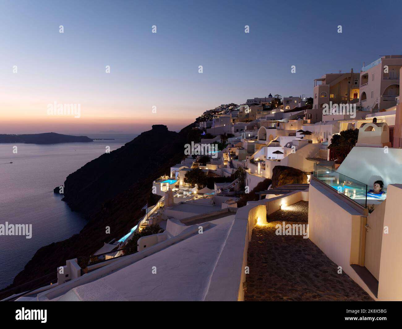 Tramonto da Fira con boutique hotel e piscine e Skaros Rock sullo sfondo, sull'isola greca delle Cicladi di Santorini. Foto Stock