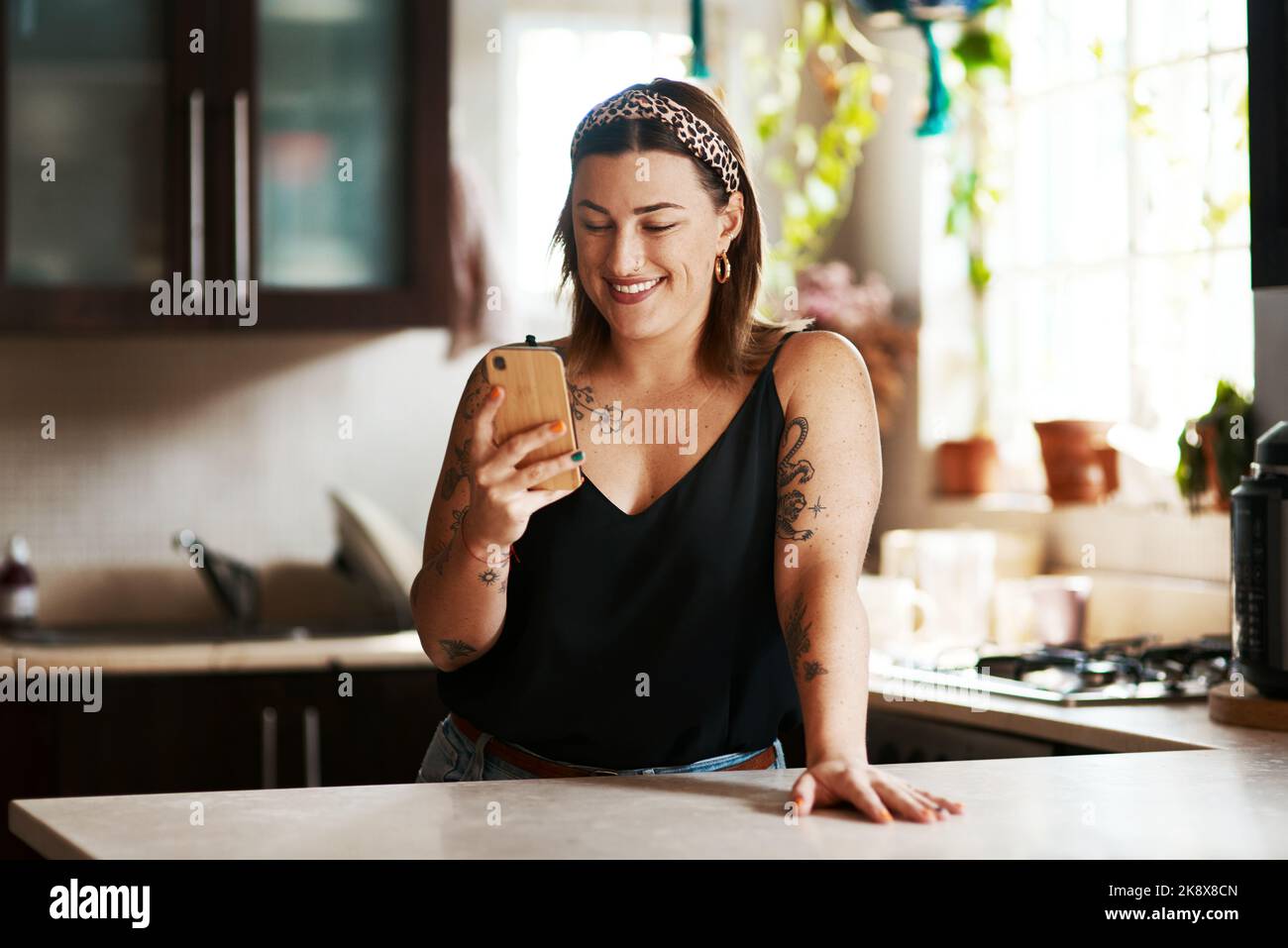 La vita sta accadendo online in questi giorni. Una giovane donna che usa uno smartphone in cucina a casa. Foto Stock