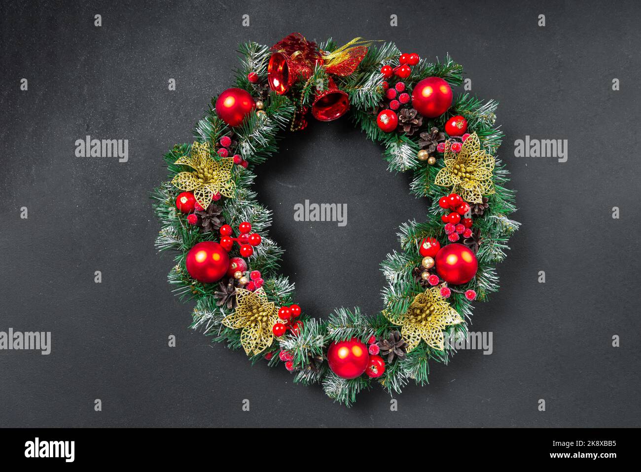 Una corona di Natale con un arco rosso e decorazioni di coni, agrifoglio, mistletoe, e verde invernale contro una porta di fronte di una quercia blu scuro. Foto Stock