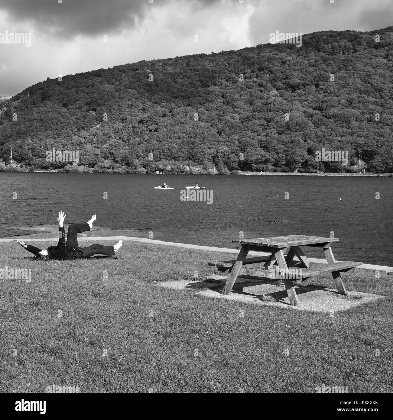Un colpo in scala di grigi di un tavolo da picnic e panca con una persona che si esercita sulla riva di Llynnau Mymbyr Foto Stock