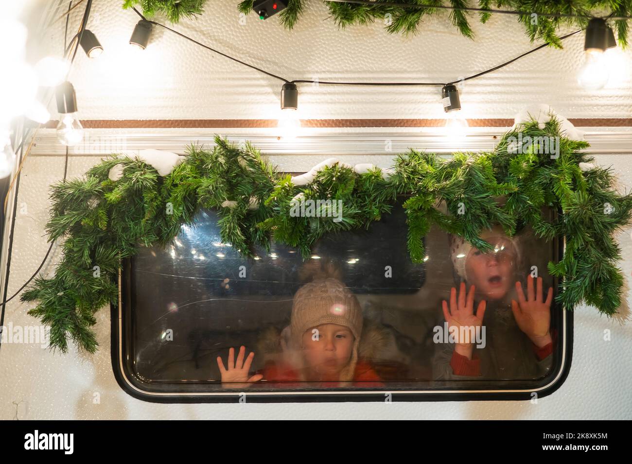 Due ragazzi guardano fuori dalla finestra di un camper decorato a Natale. Foto Stock
