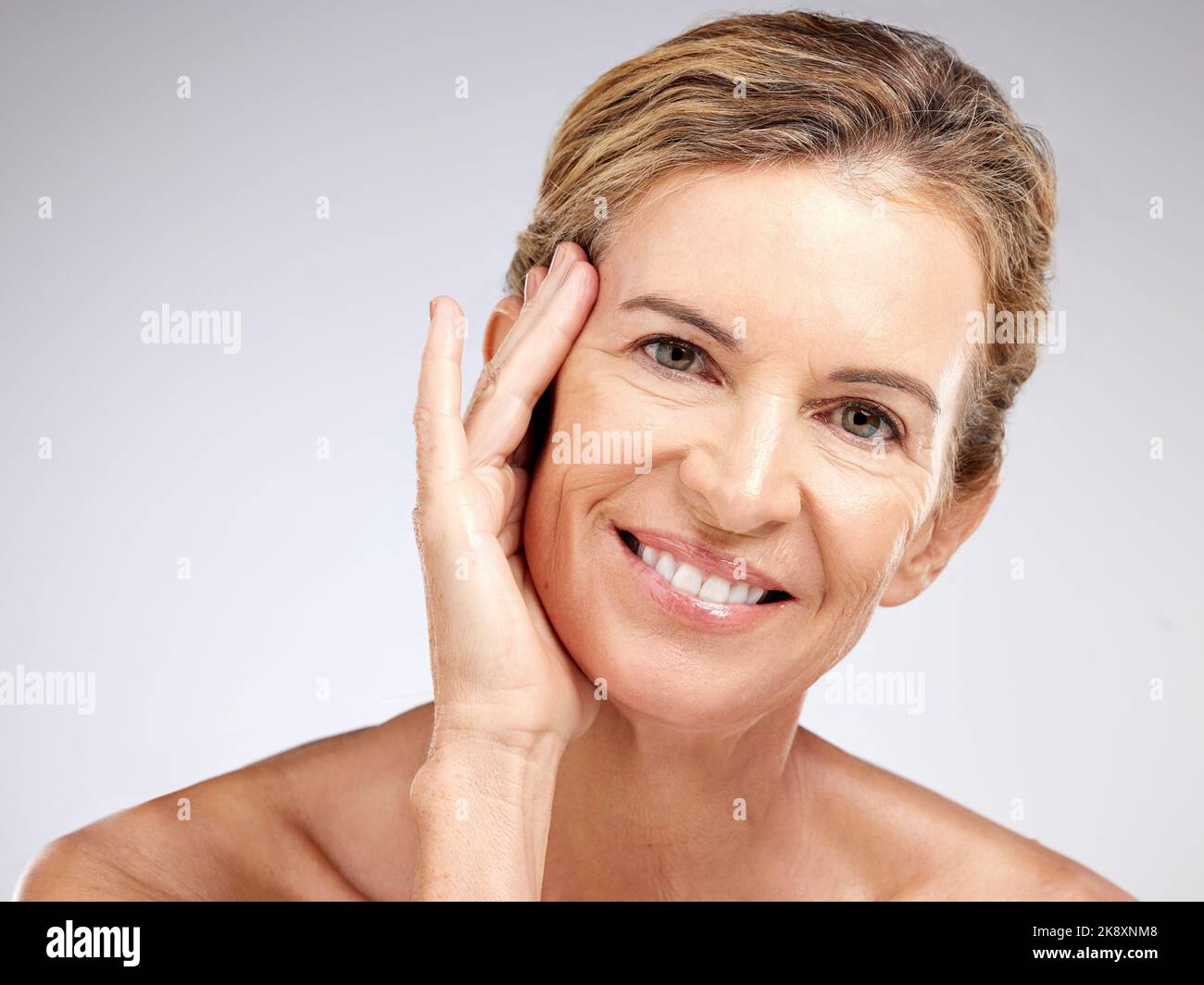 Donna anziana, bellezza e mano su faccia su sfondo grigio studio. Ritratto, modello skincare e sorriso di donna felice dal Canada con bella luce Foto Stock