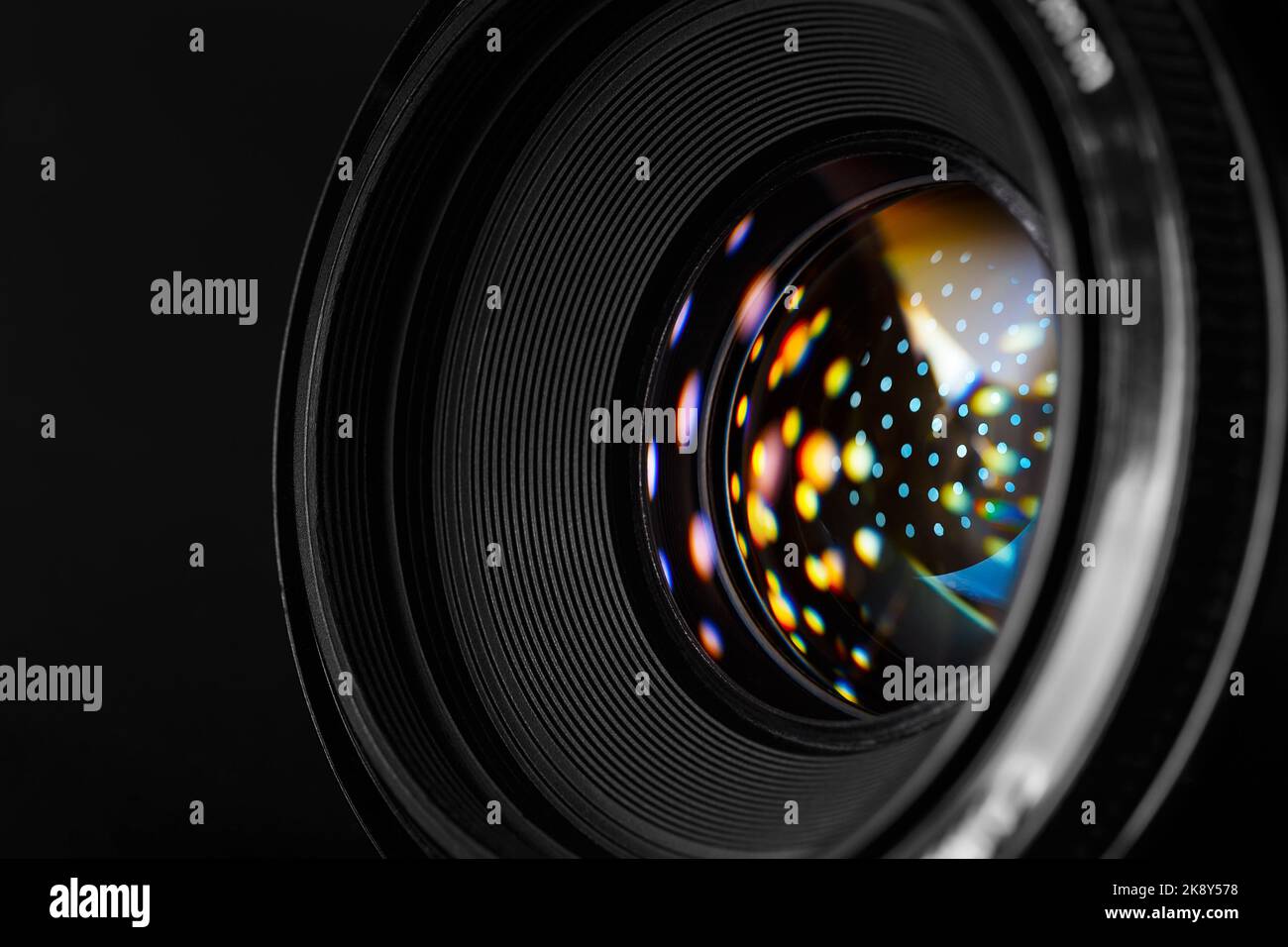 Obiettivo fotografico per primo piano, con macchie riflettenti multicolore sulla superficie dell'obiettivo anteriore. Fotografia macro in stile scuro Foto Stock