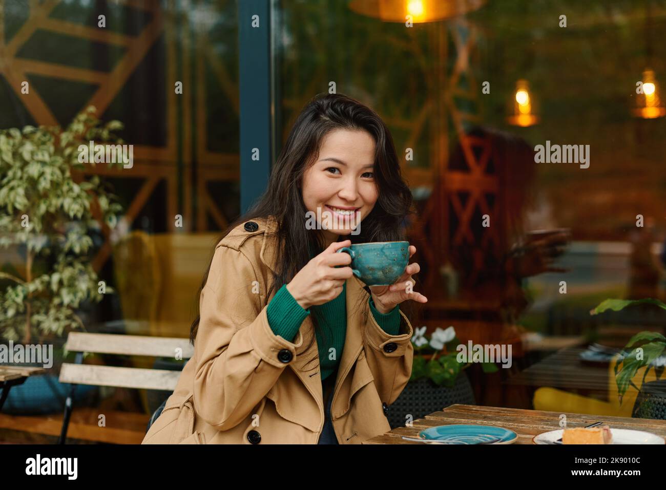 Ritratto giovane donna asiatica bere caffè in caffè sulla terrazza del caffè. All'aperto. Accogliente stagione autunnale Foto Stock