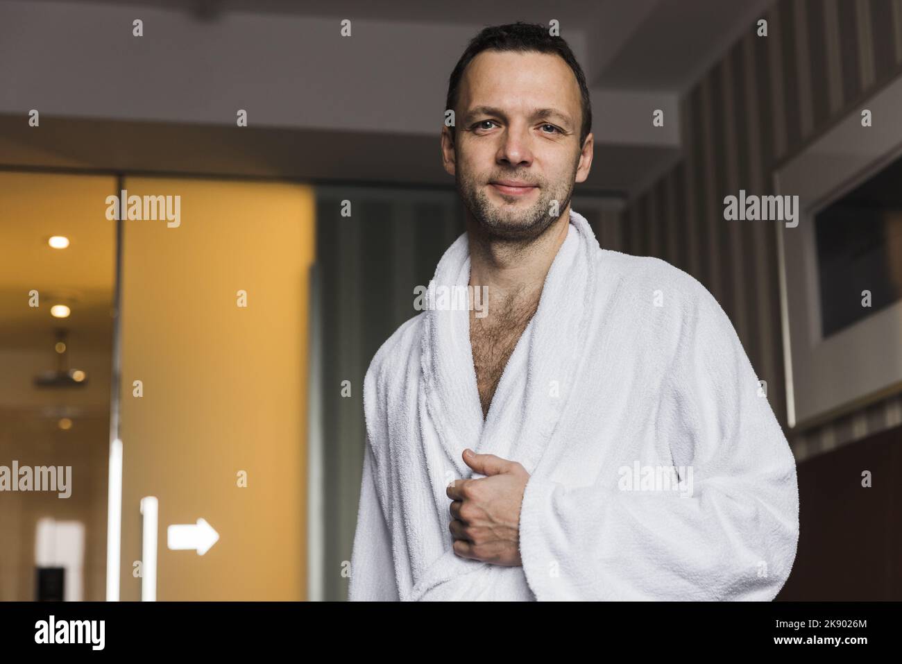 Giovane uomo caucasico sorridente in un accappatoio di cotone bianco in piedi in una camera d'albergo Foto Stock