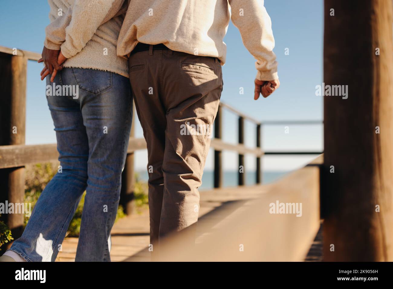 Vista posteriore di una coppia matura che tiene le mani mentre prende una passeggiata lungo un ponticello del piede di legno. Romantica coppia anziana fare una rinfrescante vacanza al mare af Foto Stock