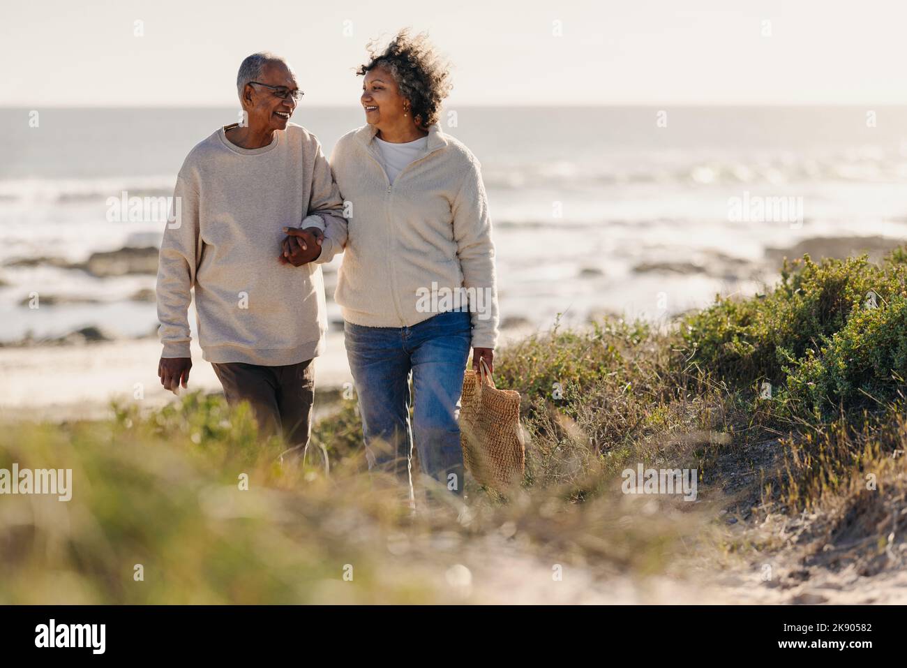 Coppia matura sorridente felicemente mentre cammina via dalla spiaggia dopo un picnic romantico. Allegra coppia anziana che si gode una vacanza al mare dopo reti Foto Stock