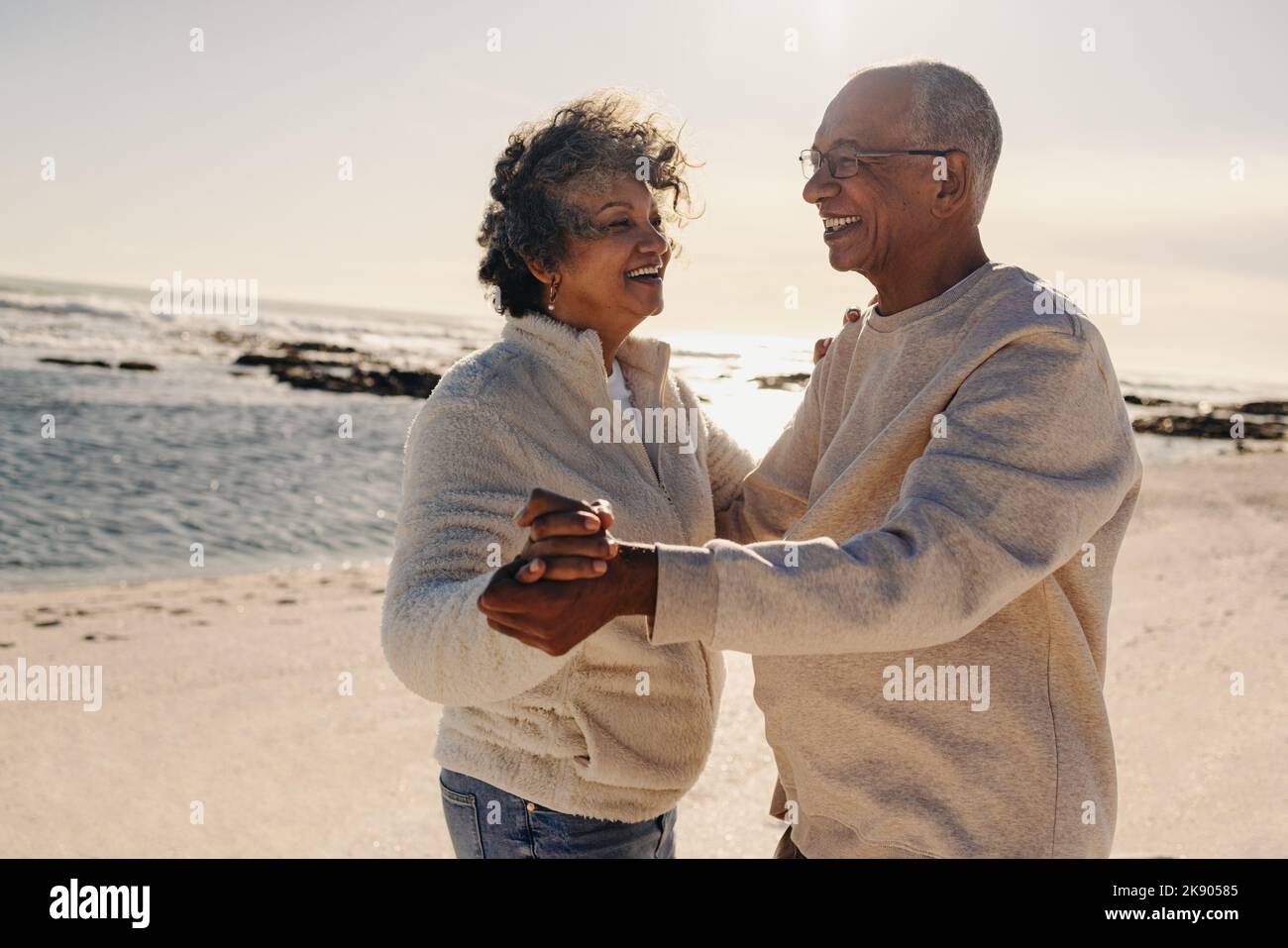 Coppia anziana sorridente mentre ballava insieme in spiaggia. Felice coppia anziana che si trova vicino all'oceano. Coppia matura allegra godendo Foto Stock