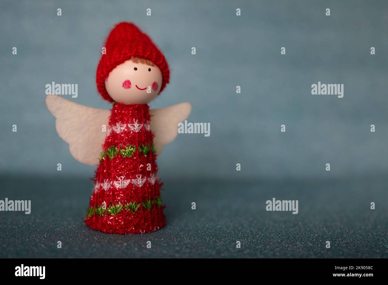 Un grazioso angelo di Natale figurina con ali bianche e un cappello rosso su uno sfondo blu pastello sfocato. Sfondo di Natale con spazio vuoto per il testo Foto Stock