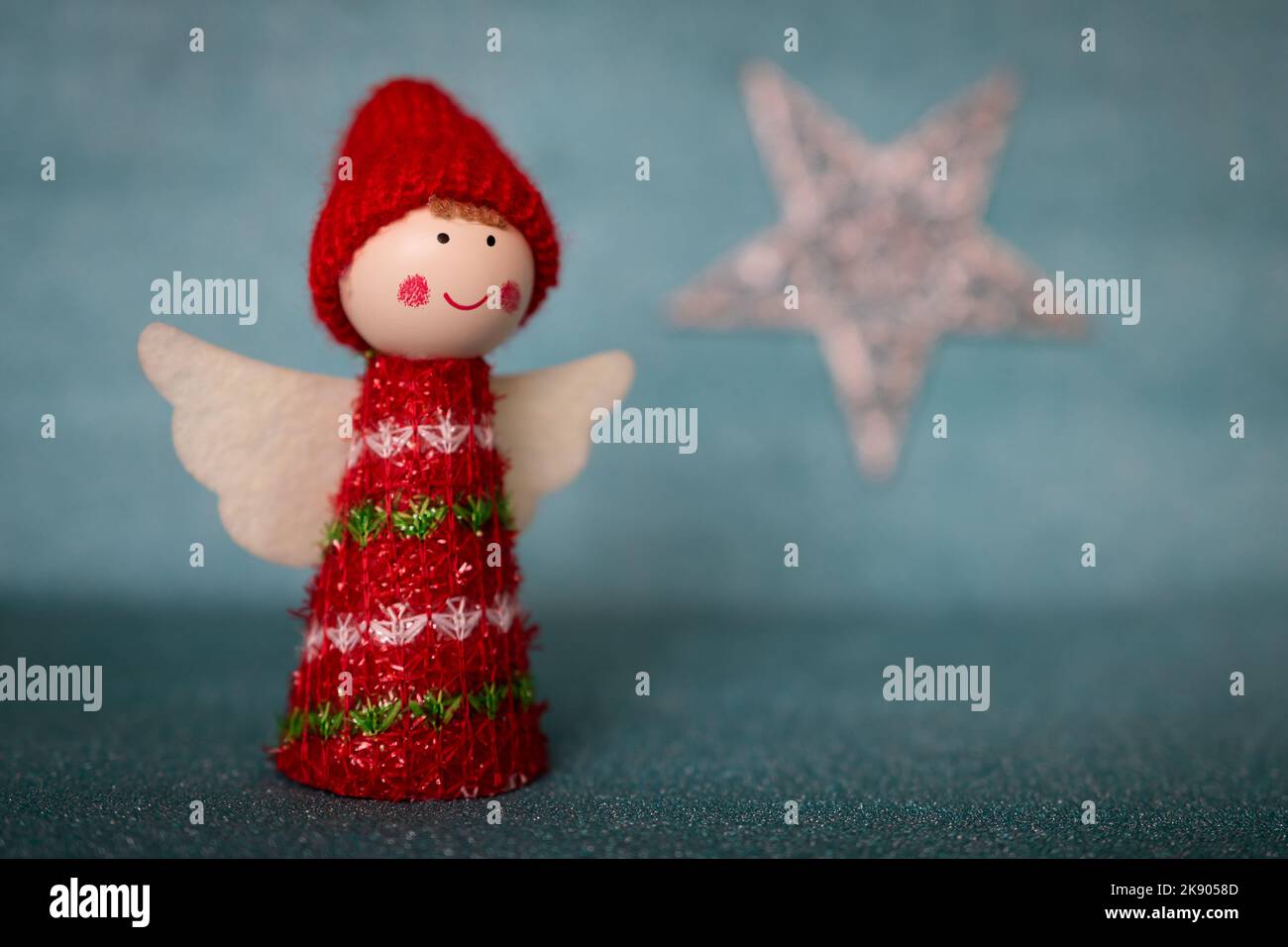 Un grazioso angelo di Natale figurina indossando un cappello rosso e vestiti con una forma a stella sfocata su uno sfondo blu. Semplice sfondo di Natale Foto Stock
