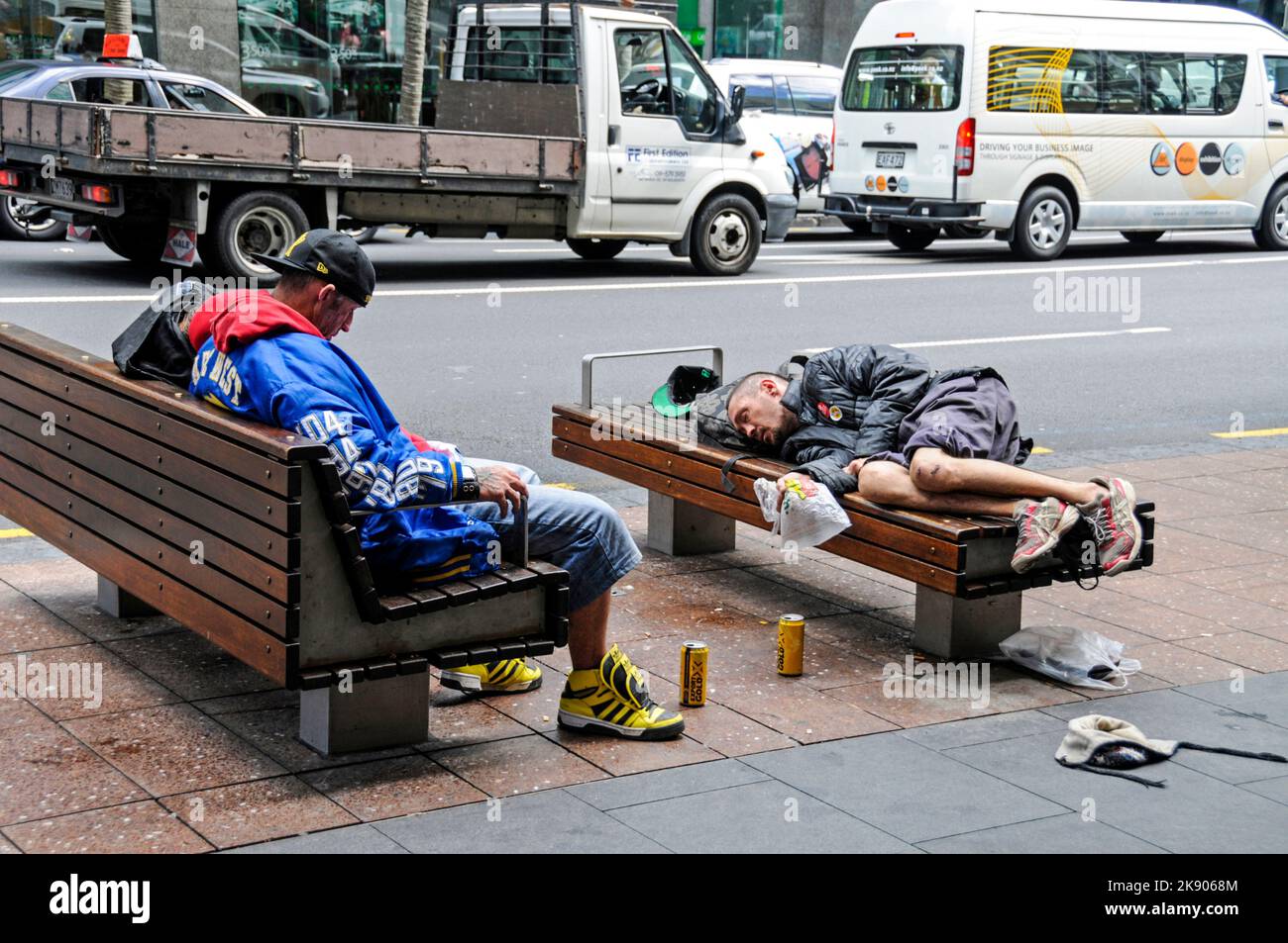 Dormendo fuori sulle panchine di strada sono due giovani uomini con le loro lattine di birra dopo un binge pesante bere in Queen Street, Auckland, Nuova Zelanda Foto Stock