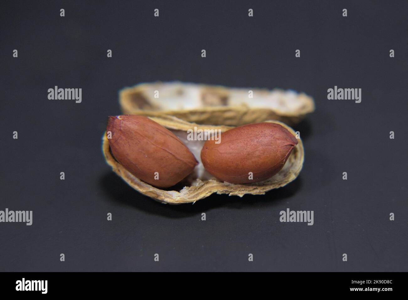 Arachidi sgusciate incrinate con due dadi all'interno su una superficie nera Foto Stock