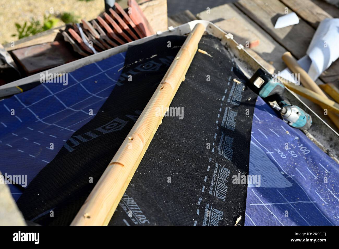 Lavori di copertura su argilla tegola residenziale Hipped Bay tetto, montaggio di membrana di sfiato sotto l'anca rafter che avrà piombo lampeggiante Foto Stock