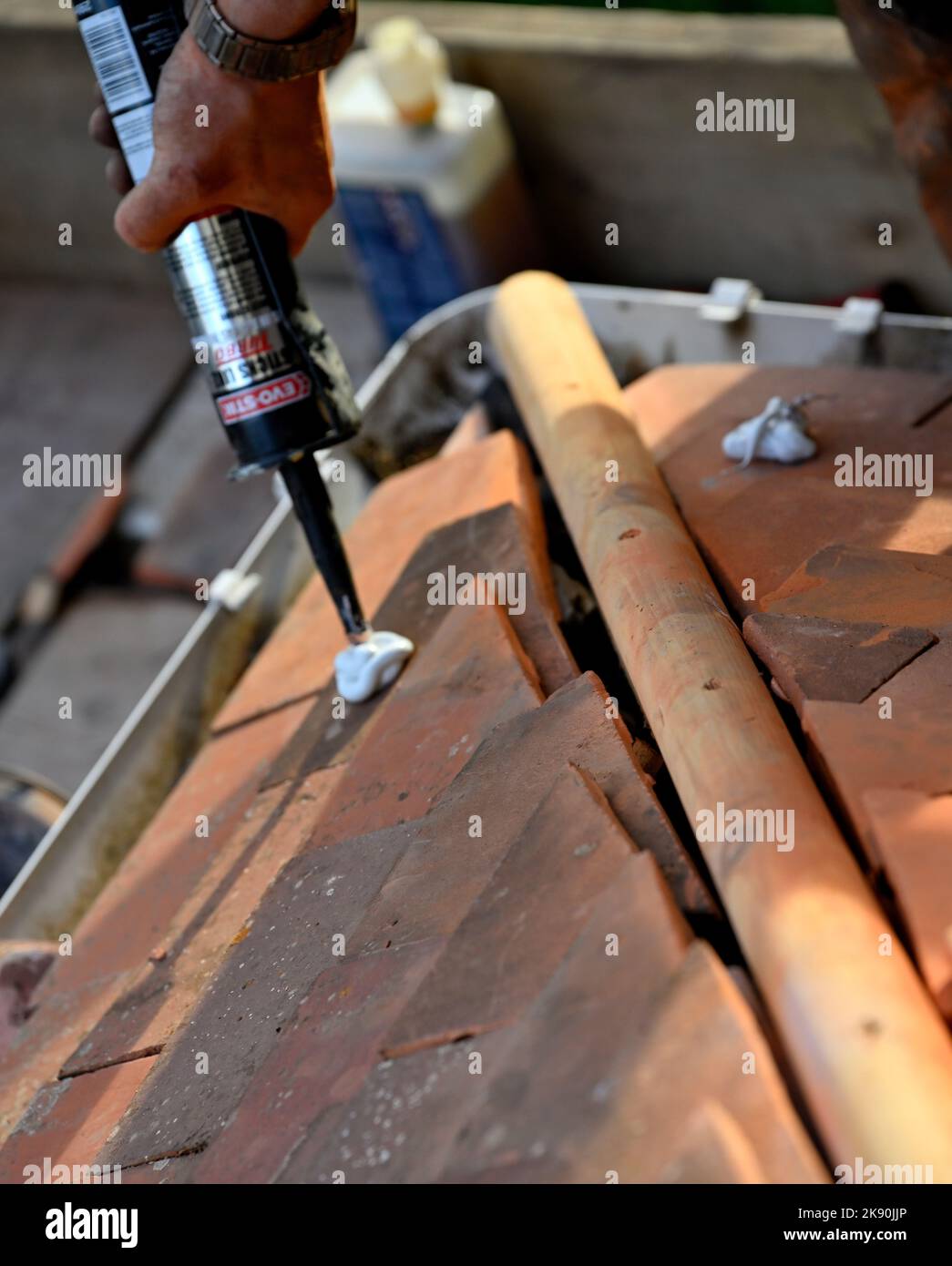 Lavori di copertura su tegole di argilla residenziale hipped Bay tetto, applicando adesivo per tenere le tegole tagliate per il montaggio angolo taglio alla caraffa Foto Stock