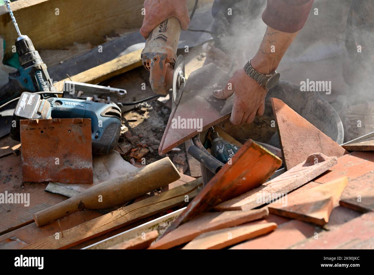 Lavori di copertura su tegole di argilla residenziale hipped Bay tetto, taglio tegole di argilla con smerigliatrice angolare Foto Stock