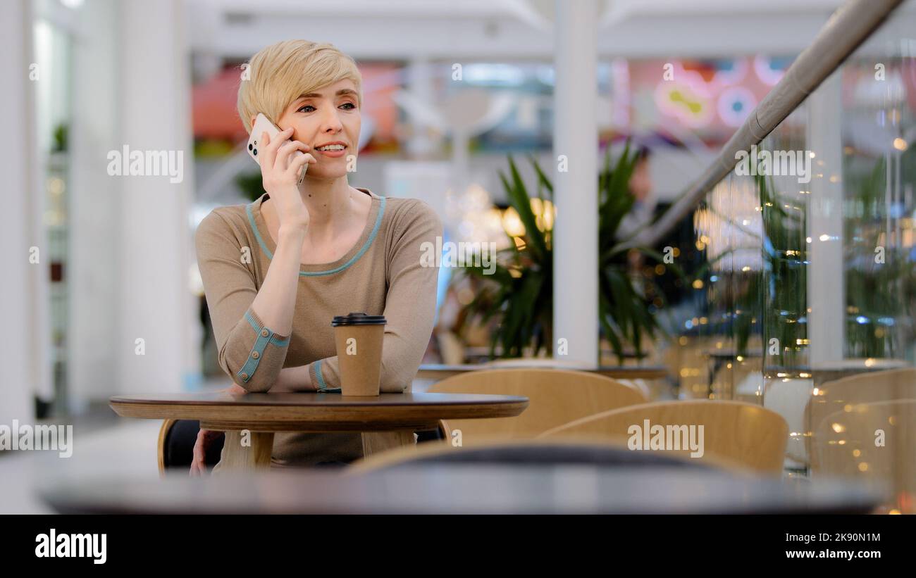 Caucasico adulto maturo di mezza età 40s donna donna d'affari donna seduta al tavolo in caffetteria parlare sul telefono cellulare smartphone risposta chiamata ordine online Foto Stock