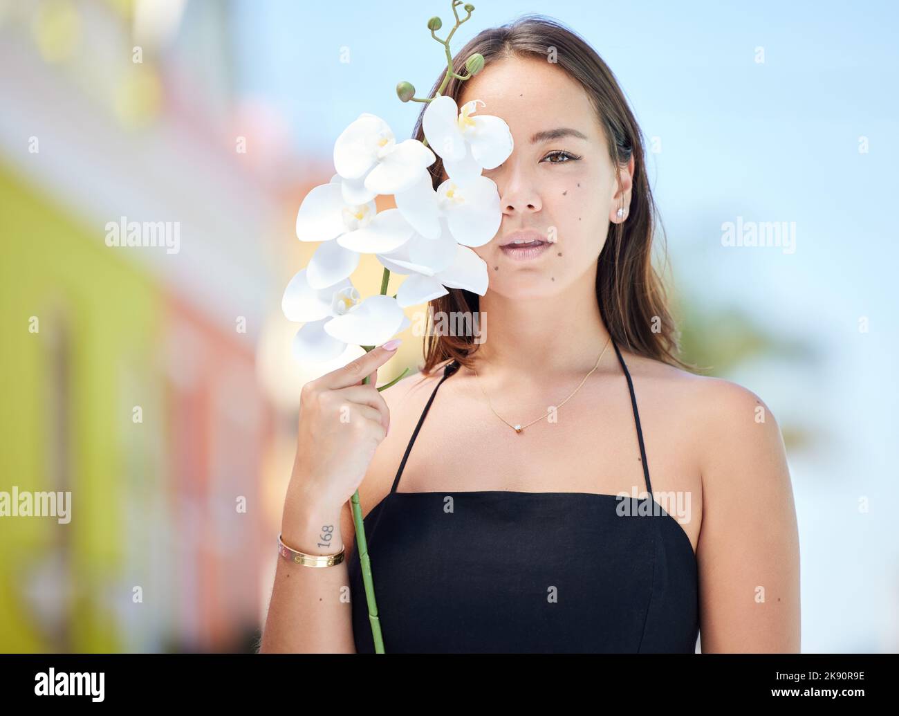 Bellezza, fiore e ritratto di ragazza in città in piedi in strada urbana, orchidea in mano. Moda, cosmetici e shot creativo di giovane donna asiatica con Foto Stock