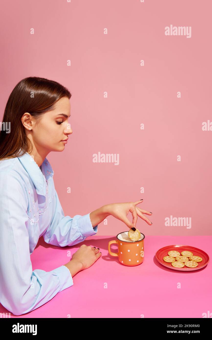 Goodies. Fotografia di arte pop del cibo. Giovane ragazza che assaggia latte con cracker isolato su sfondo rosa. Concetto di cibo, creatività. Foto Stock