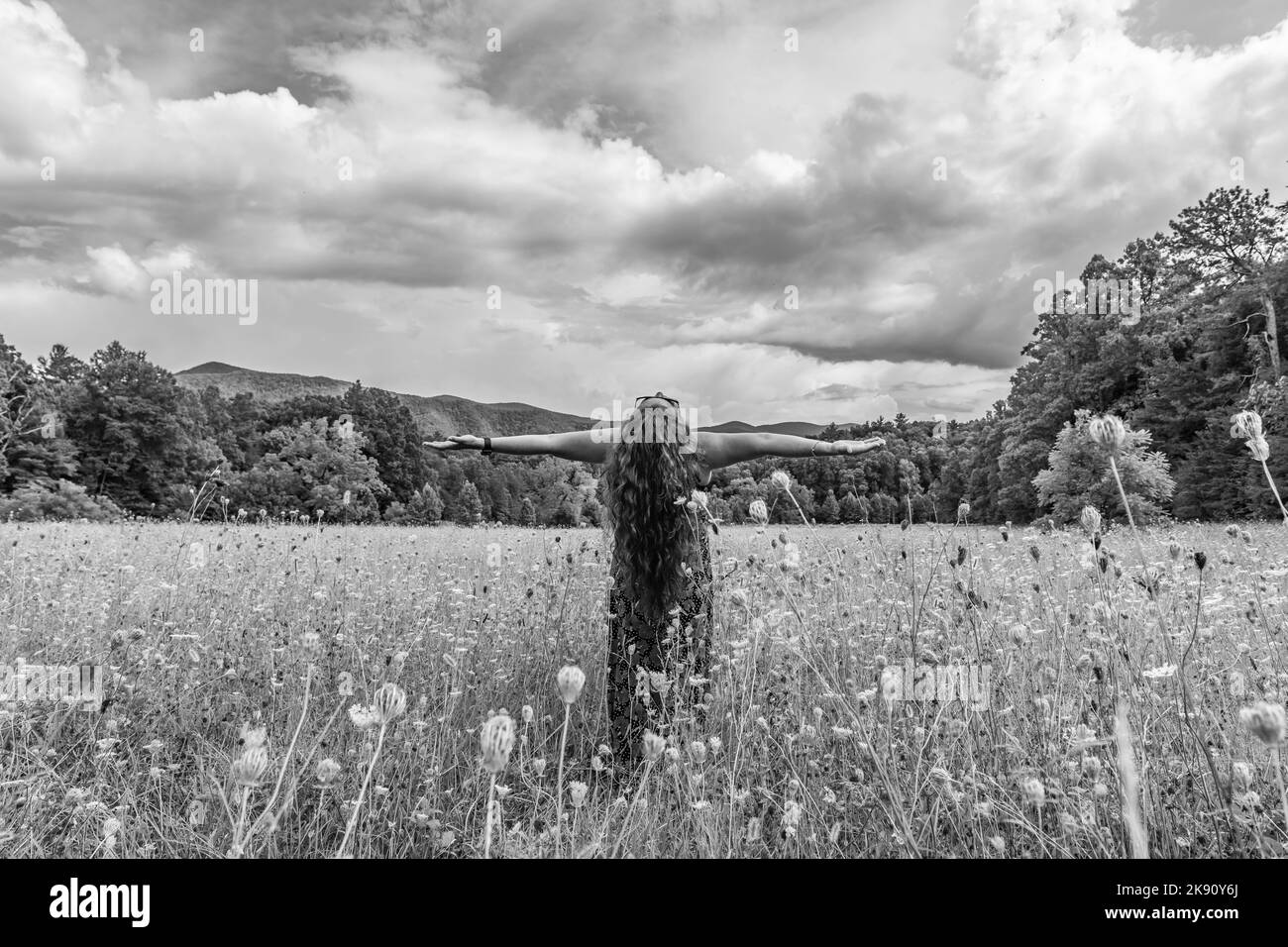 Una scala di grigi di una donna soddisfatta della natura, sia la testa che le braccia alzate Foto Stock
